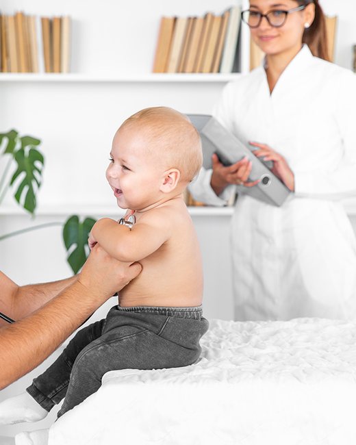 Doctor listening to a smiling baby's chest while a colleague takes notes