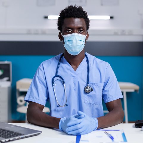 Nurse in a mask and scrubs ready to help at the clinic desk