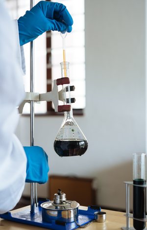 Gloved hand adjusting a round-bottom flask on a lab stand